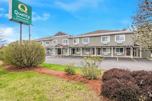 A hotel with a green sign, multiple rooms, and a parking lot.