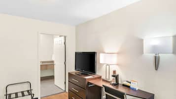 Habitación de hotel con escritorio, televisión, lámpara, silla y cafetera.