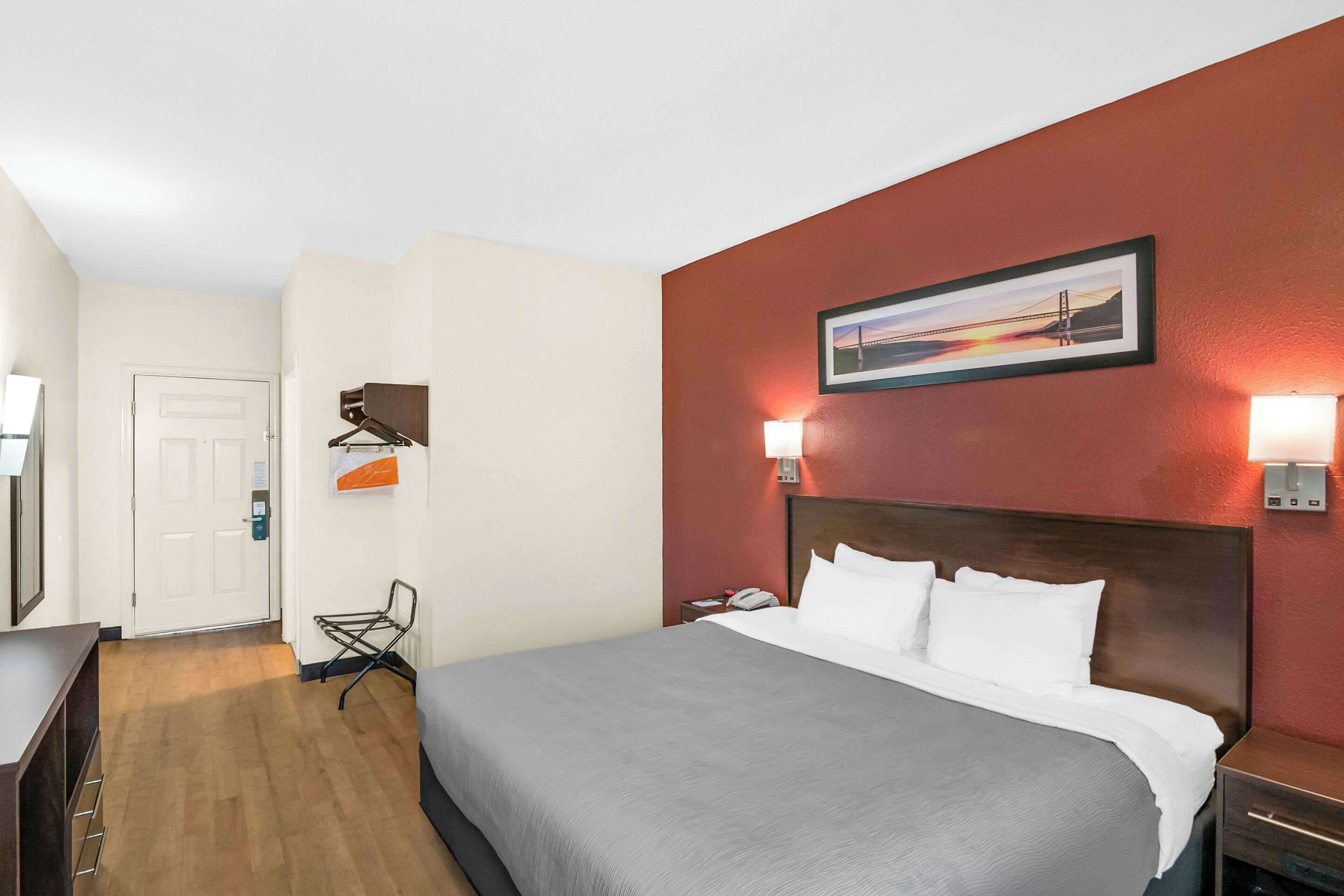 Une chambre d’hôtel avec un lit, une table de chevet, une lampe, une chaise et une porte.