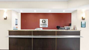 Una reception di hotel con una parete rossa a contrasto, un cartello che indica 'Quality by Choice Hotels' e un banco con un computer e un telefono.
