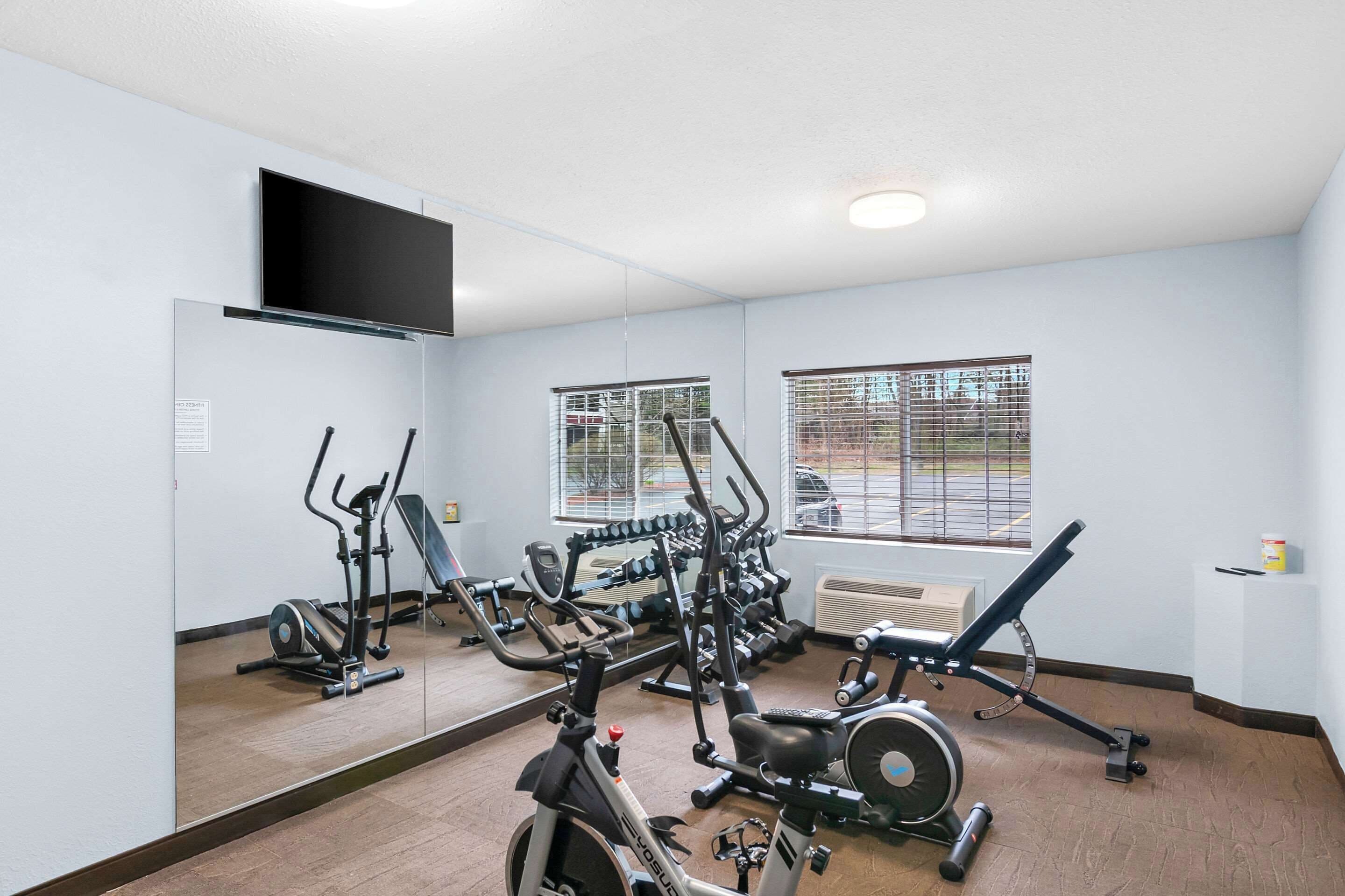 A gym with various exercise equipment, a large mirror, and windows with blinds.