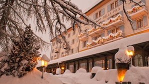 Un bâtiment recouvert de neige, orné de balcons décorés de guirlandes lumineuses, ce qui témoigne d’une période de fêtes.