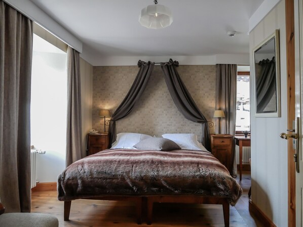 Un dormitorio con cama, cortinas, mesita de noche con lámpara, espejo y puerta.