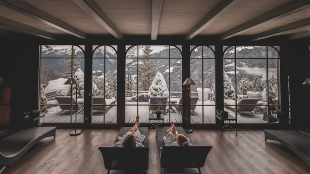 Une pièce dotée de grandes fenêtres donnant sur un paysage montagneux enneigé. Deux fauteuils sont placés face aux fenêtres.