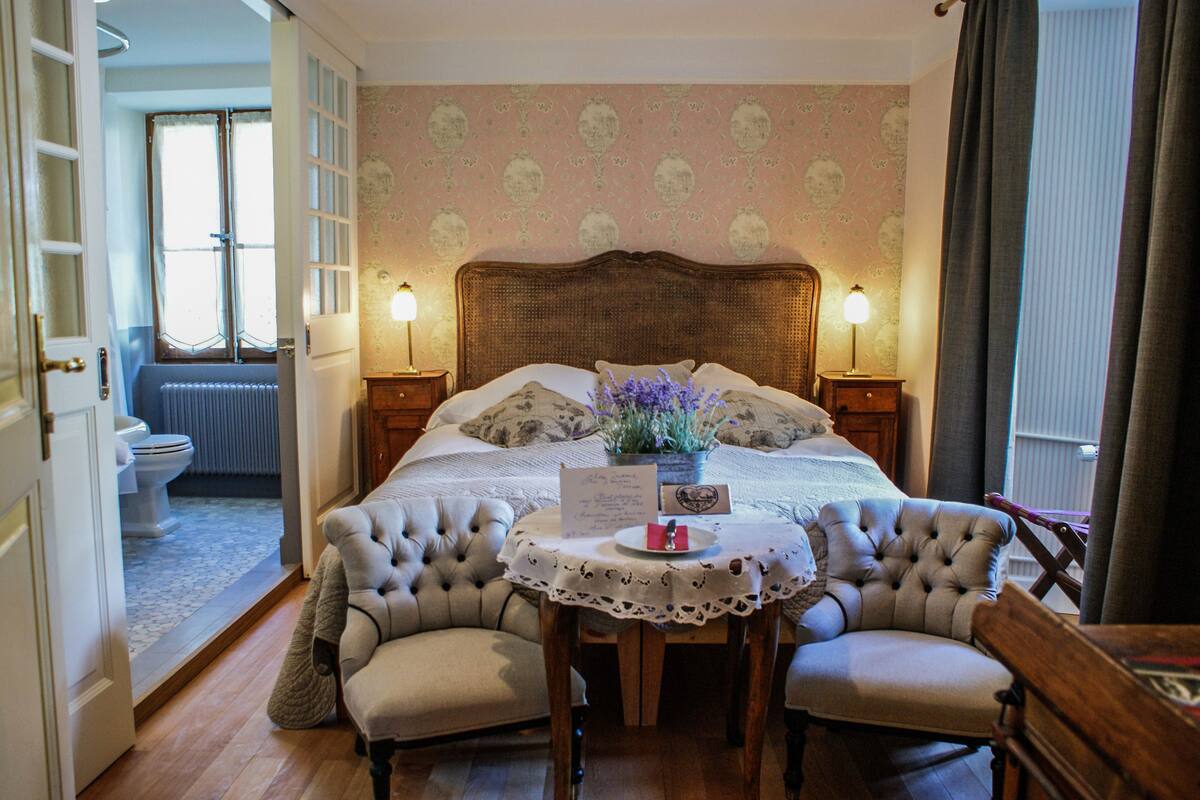 Un dormitorio con una cama grande, mesitas de noche, una pequeña mesa con un florero y una silla.