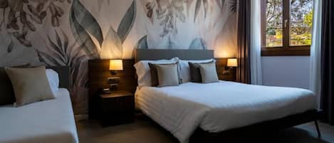 Habitación de hotel con una cama grande, dos mesitas de noche con lámparas, un mural floral en la pared y una ventana con cortinas.