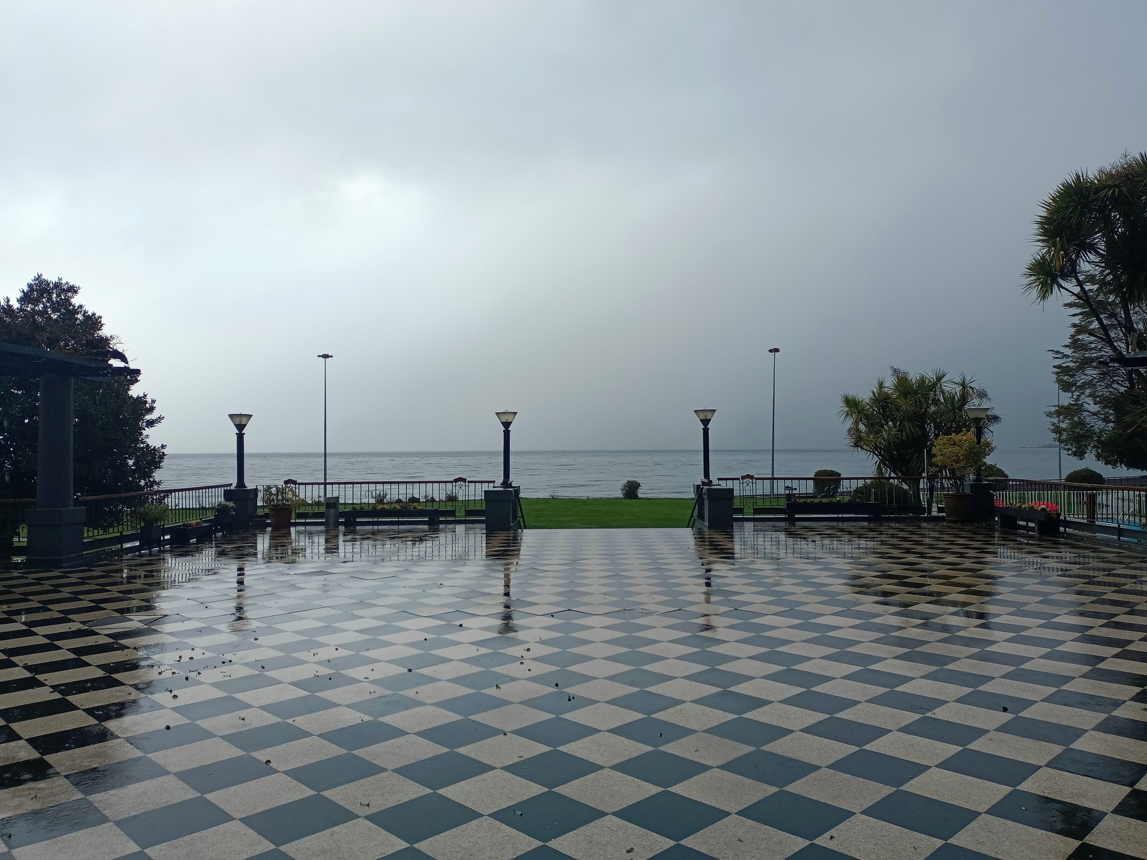A checkered outdoor area with a view of the sea, benches, and street lamps.