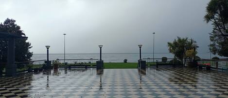 A checkered outdoor area with a view of the sea, benches, and street lamps.