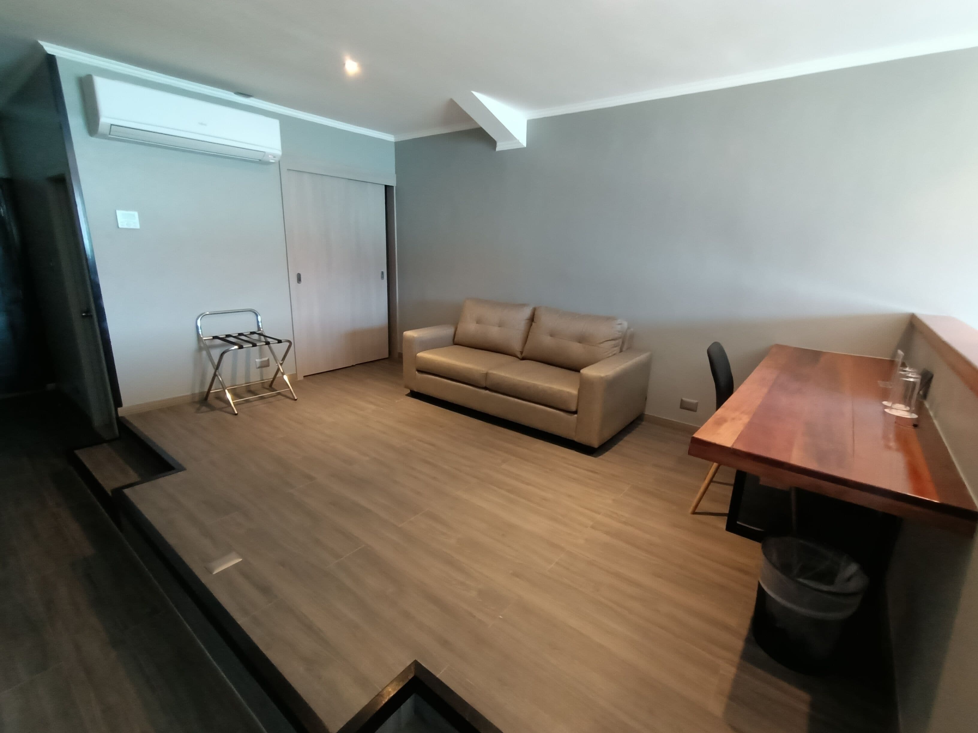 A modern living room with a beige sofa, a wooden dining table, and a small black trash bin.
