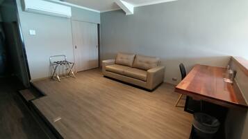 Una sala moderna con un sofá color beige, una mesa de comedor de madera y un cubo de basura negro pequeño.