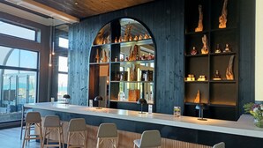 A bar area with wooden shelves displaying bottles and decorative items, a counter with stools, and large windows offering a view. - Enjoy Pucon (Pucón)