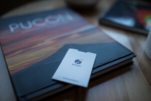 A book titled 'PUCON' with a card labeled 'enjoy' on a wooden surface.