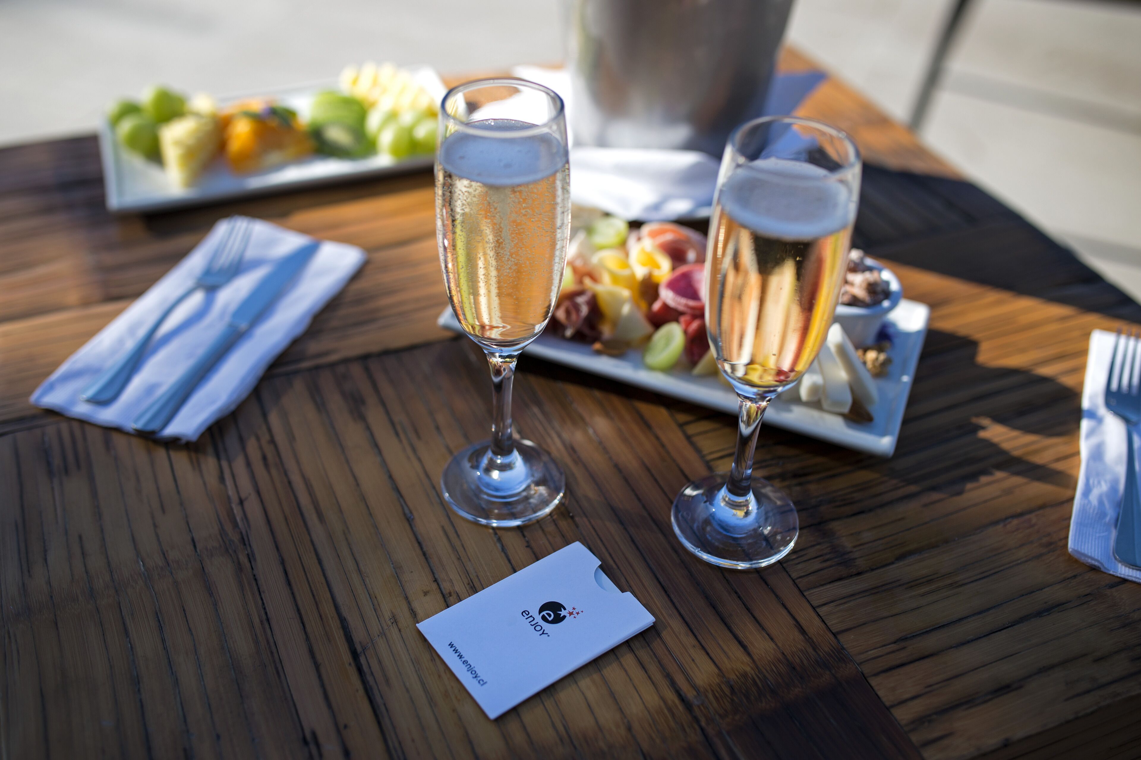 A wooden table with two glasses of champagne, a plate of fruit, and a business card.