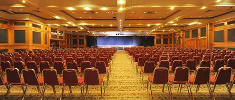 Une grande salle de conférence avec des rangées de chaises rouges et une scène à l’avant.