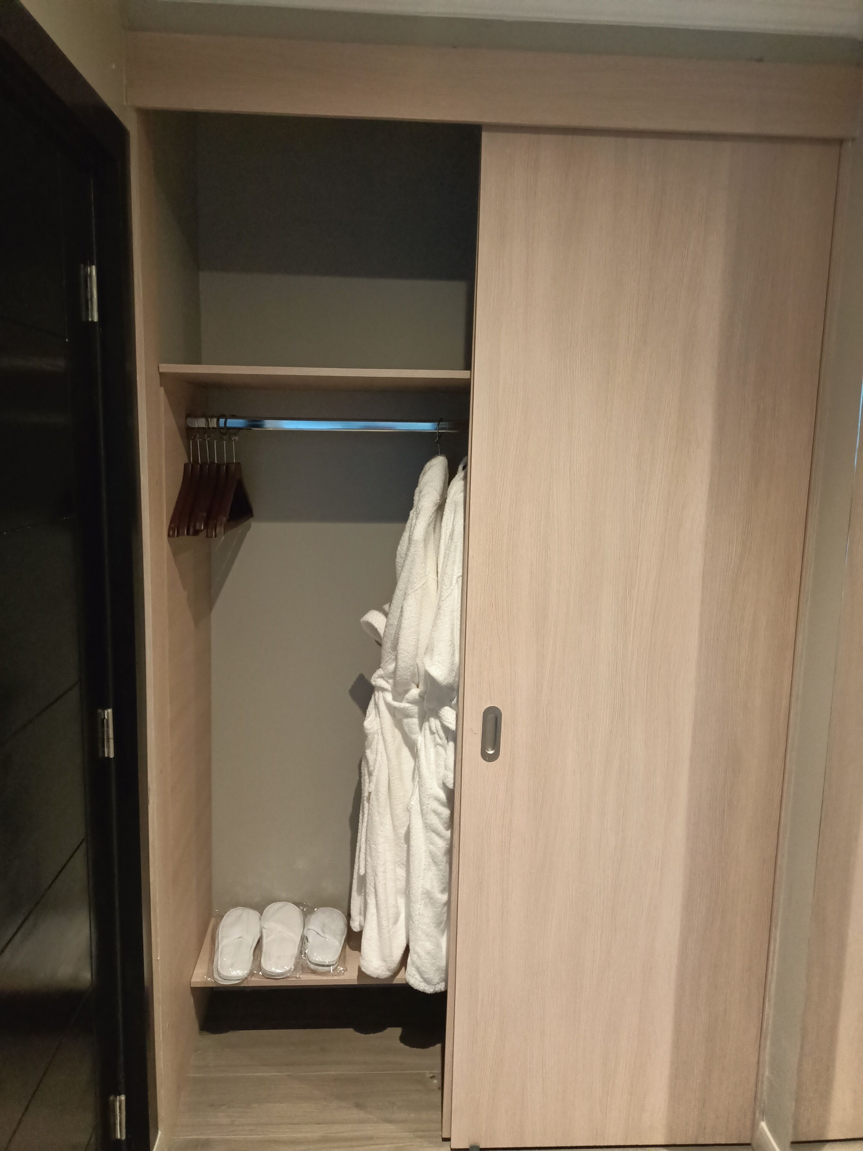 A walk-in closet with wooden doors, a shelf with shoes, and a hanging rack with towels.