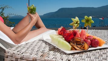 Relax in a serene beachside setting with a wicker lounge chair and refreshing treats.
