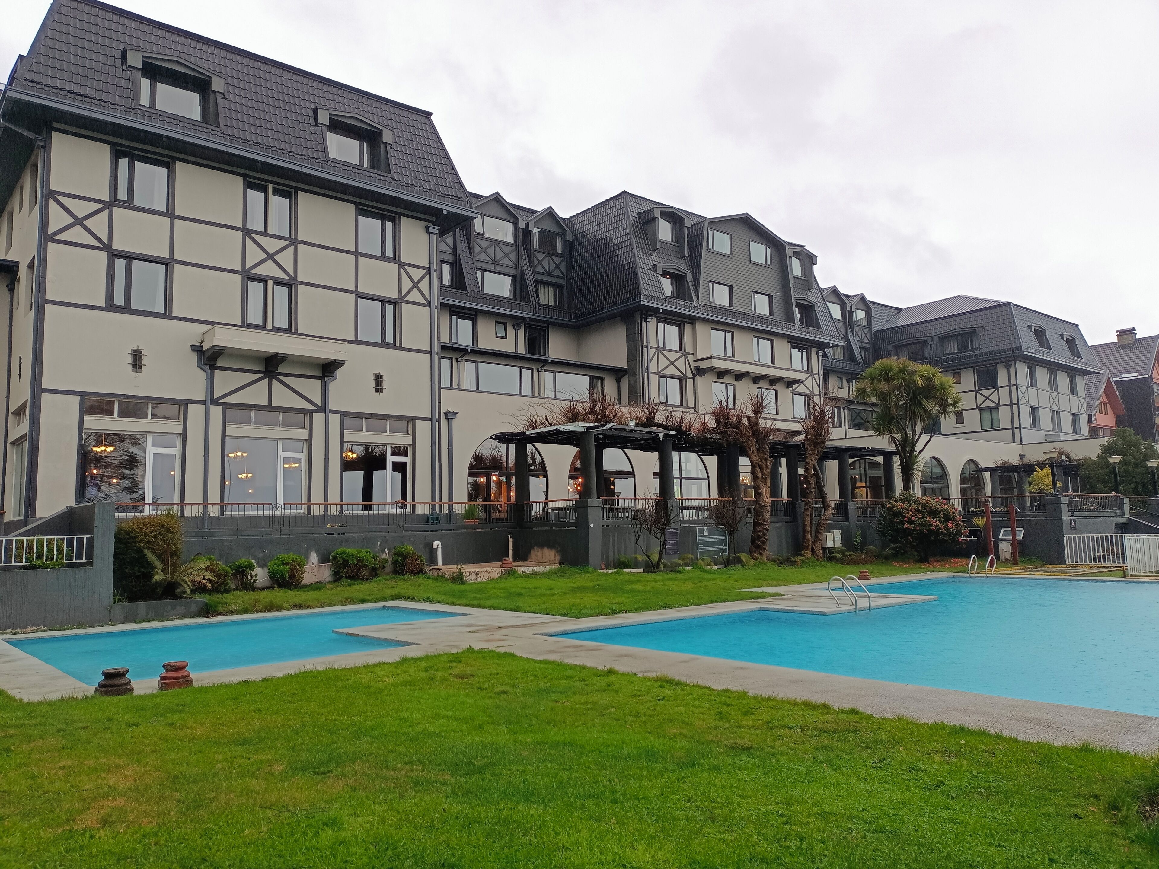 A hotel with a large outdoor swimming pool, a covered patio area, and a well-maintained lawn.