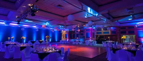 Un salón de banquetes con mesas dispuestas para un evento formal, con un techo alto e iluminación moderna.