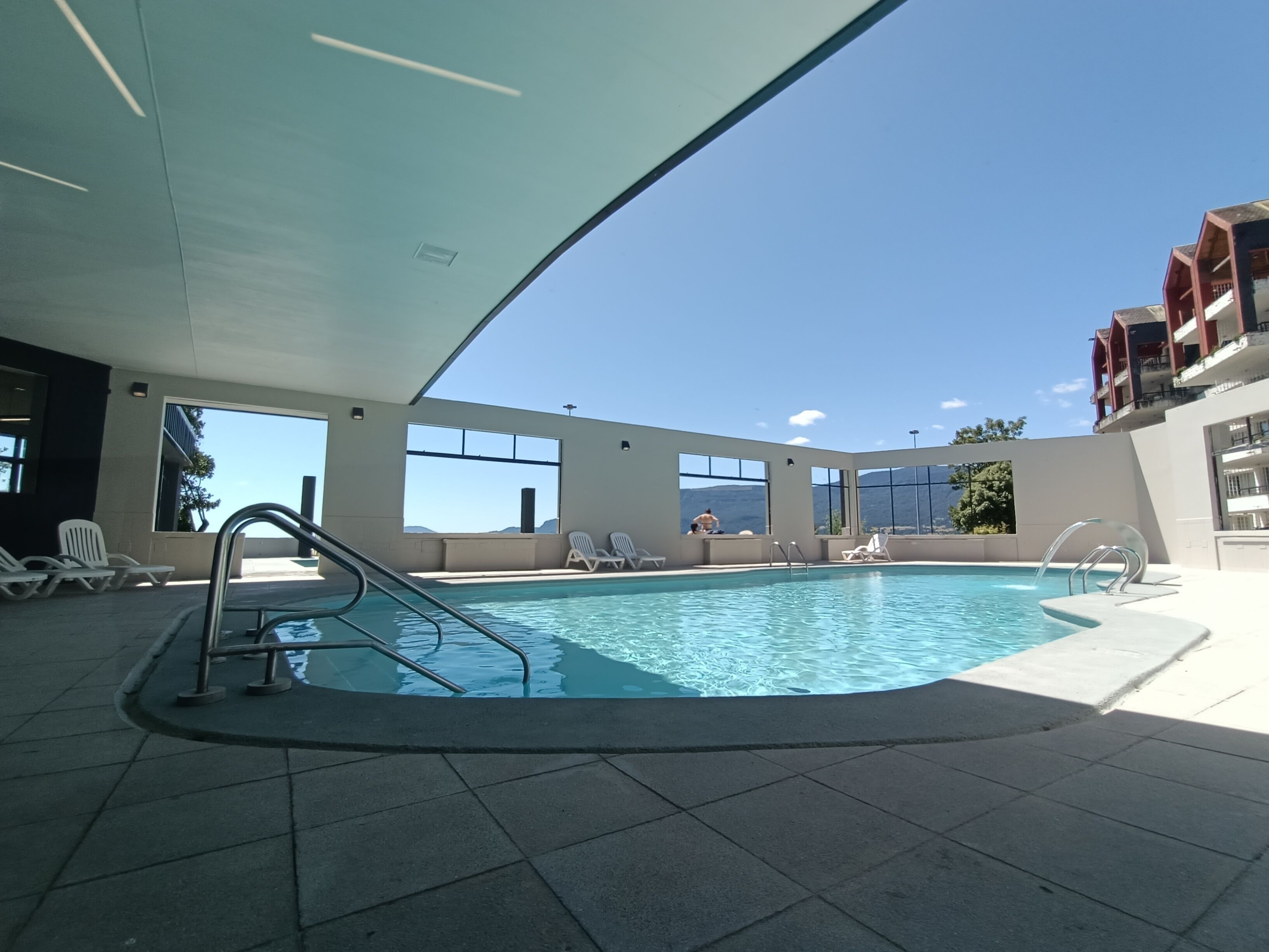 An indoor swimming pool with clear views of the mountains, surrounded by lounge chairs and large windows.