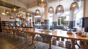 A spacious dining area with long wooden tables, hanging wicker pendant lights, and a view of the outdoors through large windows. - Enjoy Pucon (Pucón)