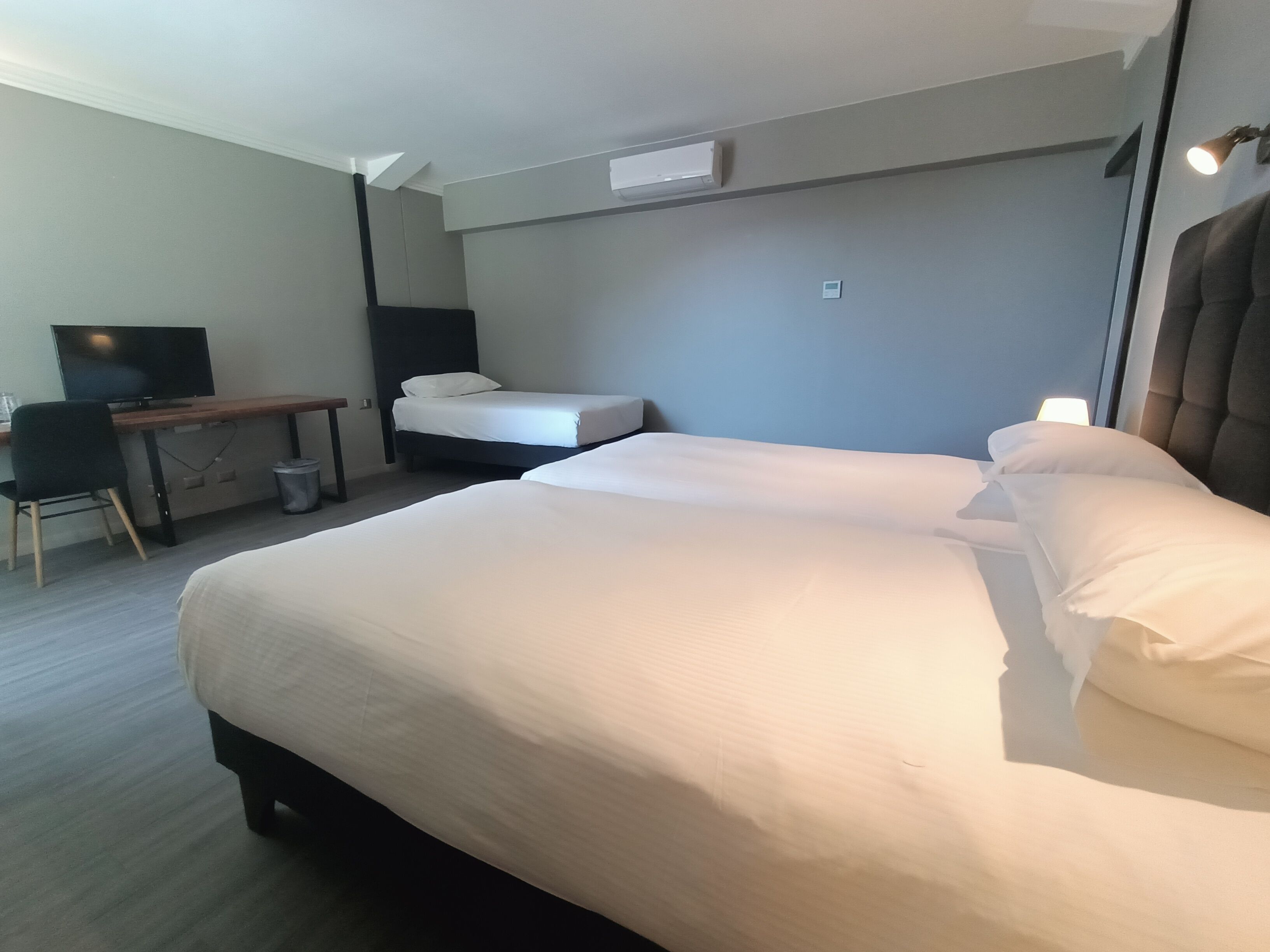 A hotel room with a large bed, a desk with a chair, a TV, and a small trash bin.