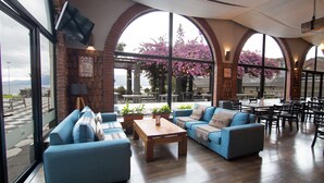 A spacious indoor area with blue sofas, a wooden coffee table, and large arched windows offering views of a garden with pink flowers. - Enjoy Pucon (Pucón)