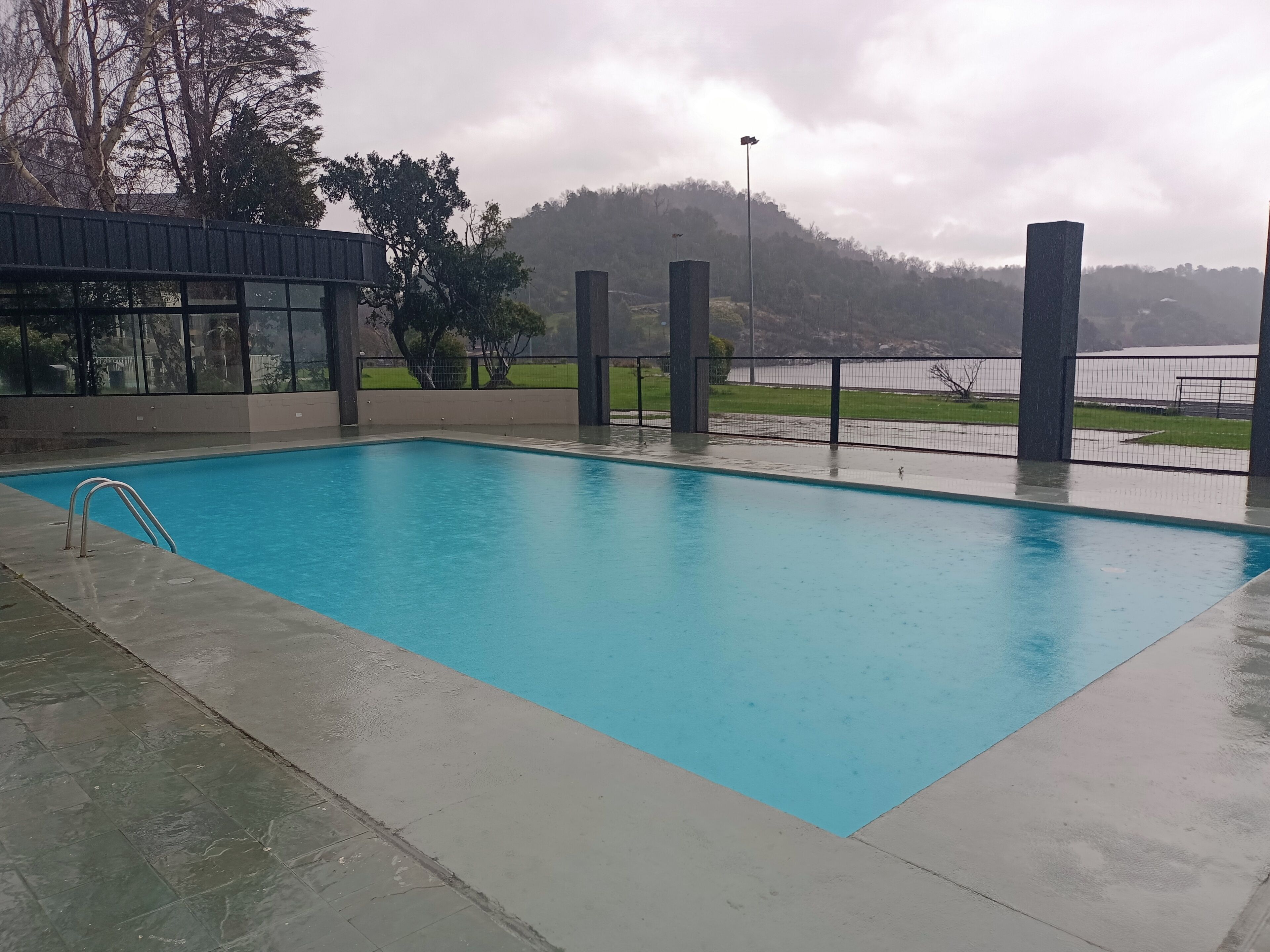 Piscina rectangular con una escalera de metal en un lateral, rodeada por una solana de hormigón.