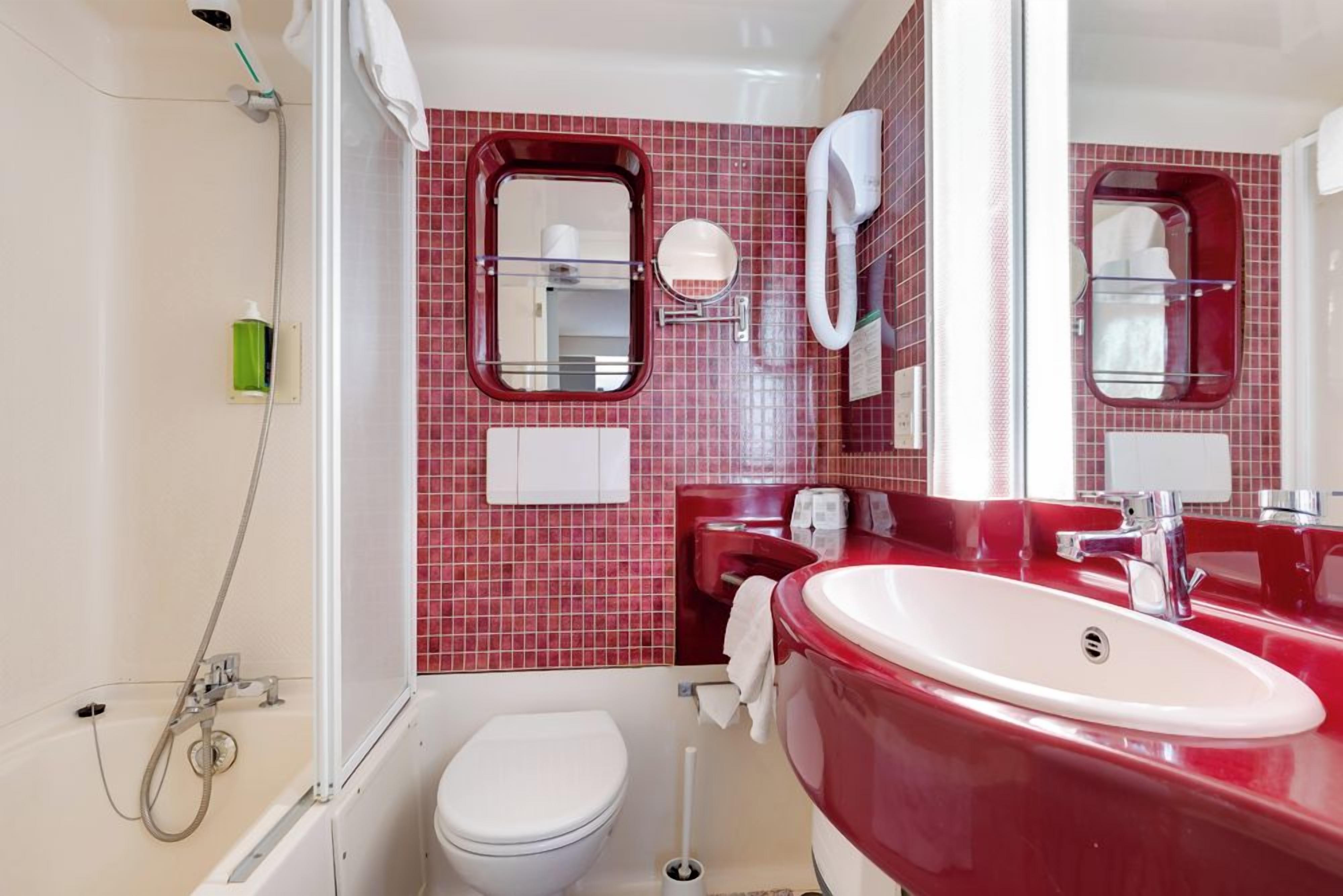 Une salle de bain avec des toilettes blanches, un lavabo rouge et un espace douche.