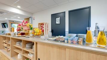 Zona de buffet per esmorzar amb diversos aliments, una cistella de fruita i un dispensador de suc.