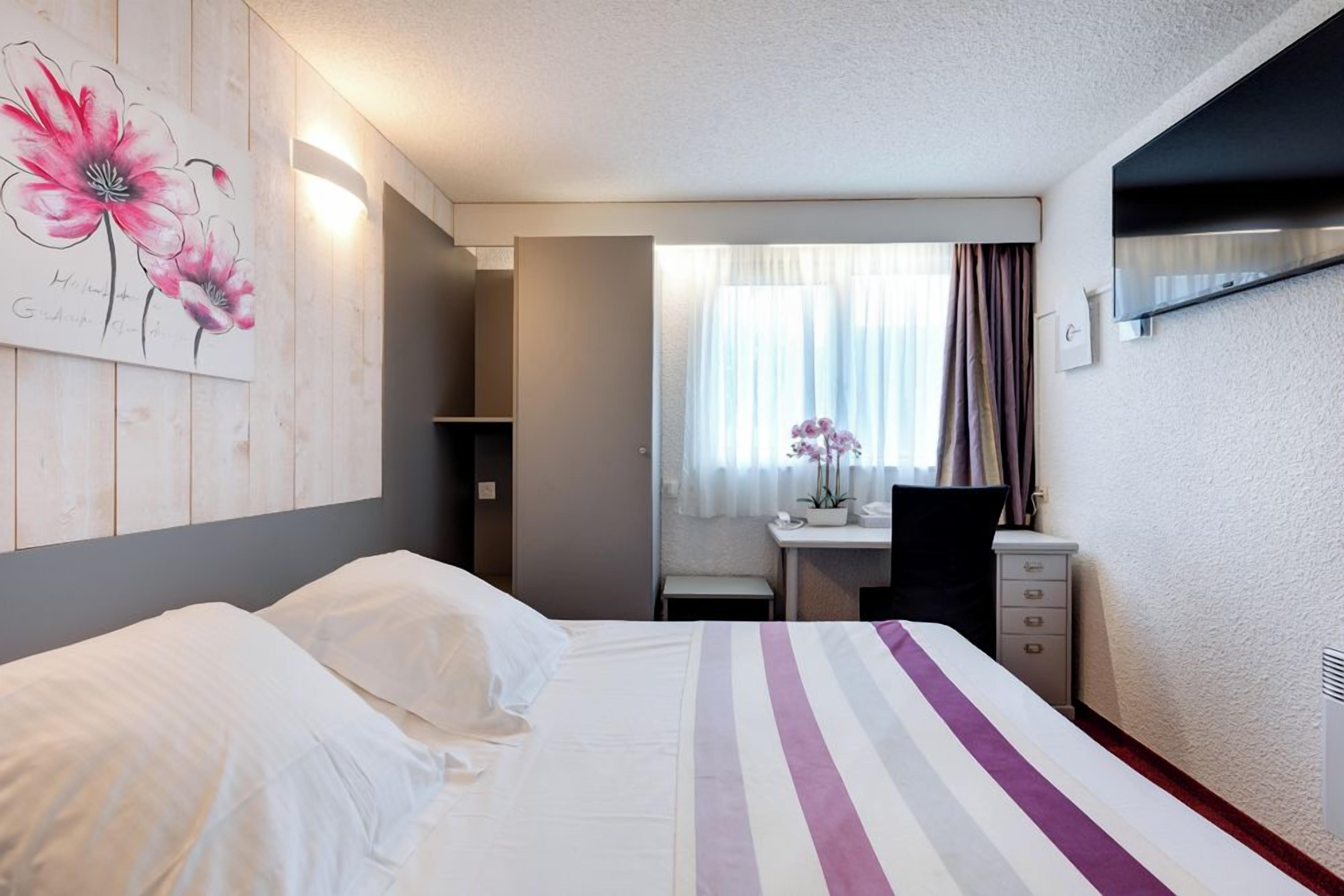 Een hotelkamer met een bed, bureau, stoel en raam met gordijnen.