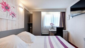 Una habitación de hotel con cama, escritorio, silla y ventana con cortinas.