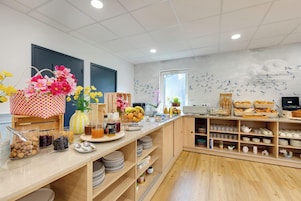 Um buffet de café da manhã com diversos alimentos e um painel decorativo na parede.