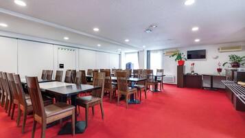 A conference room with tables and chairs, a television, and potted plants.