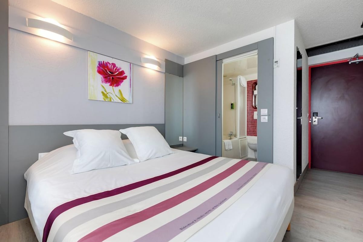 A hotel room with a bed, a mirror, a door, and a wall with a painting.