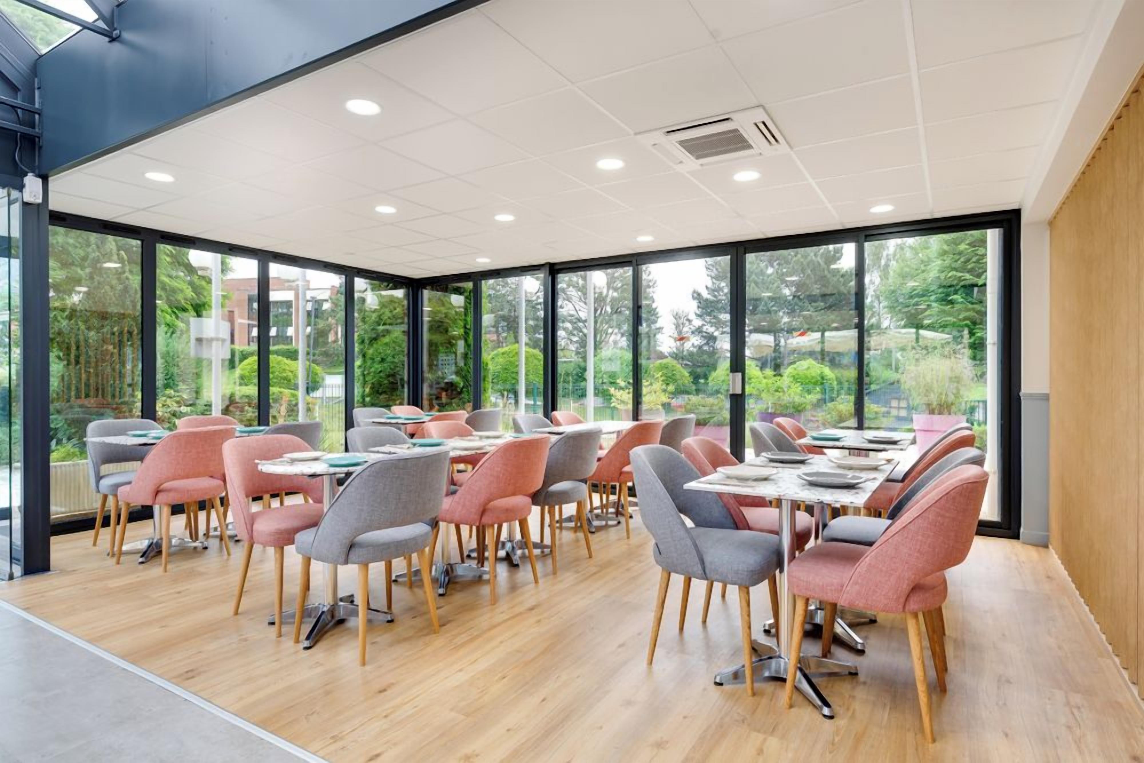 A modern conference room with large windows, wooden flooring, and a mix of grey and pink chairs.