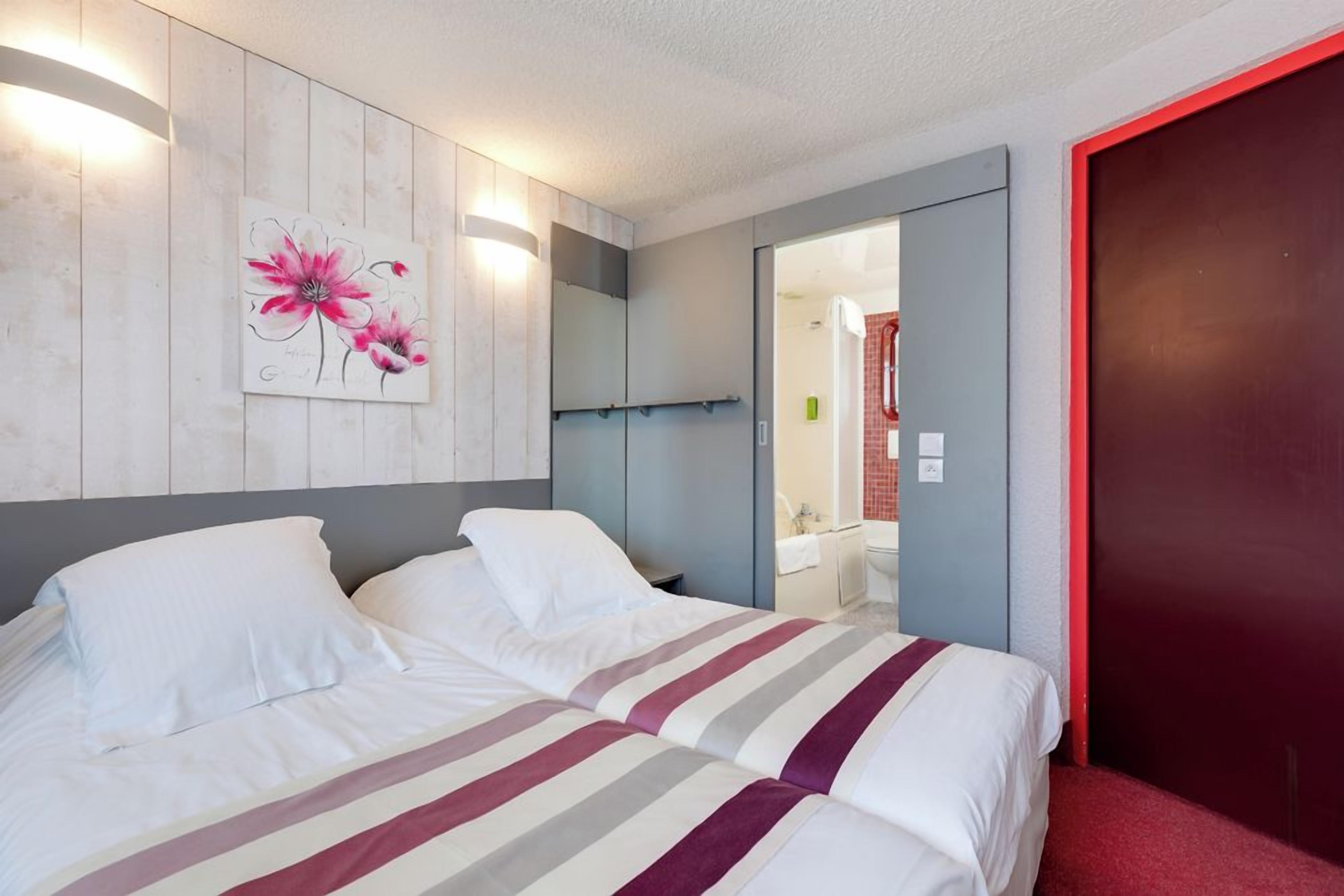 Une chambre d’hôtel avec un lit, un miroir et un tableau représentant des fleurs.