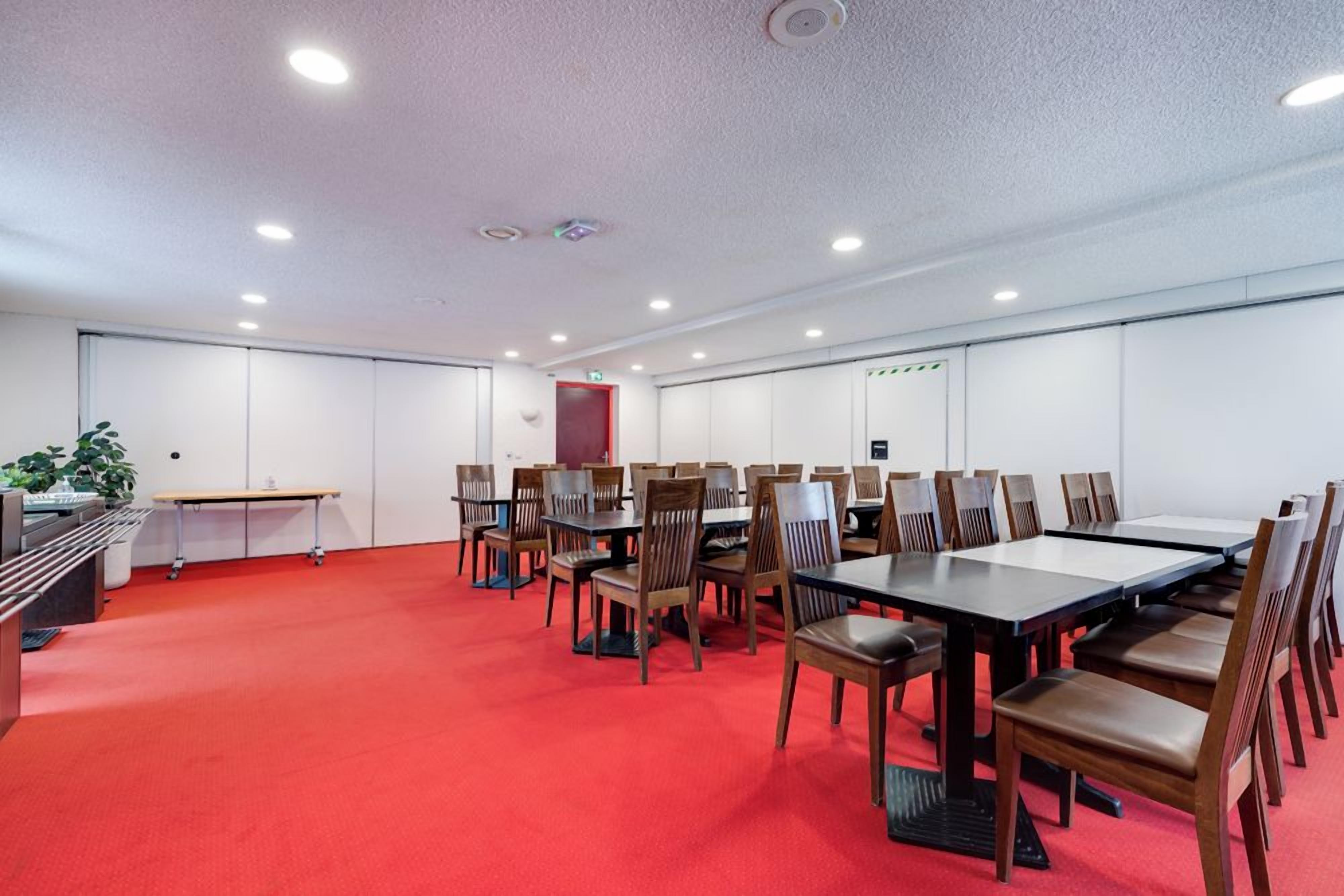 Ein Konferenzraum mit mehreren Tischen und Stühlen, einem roten Teppichboden und weißen Wänden.