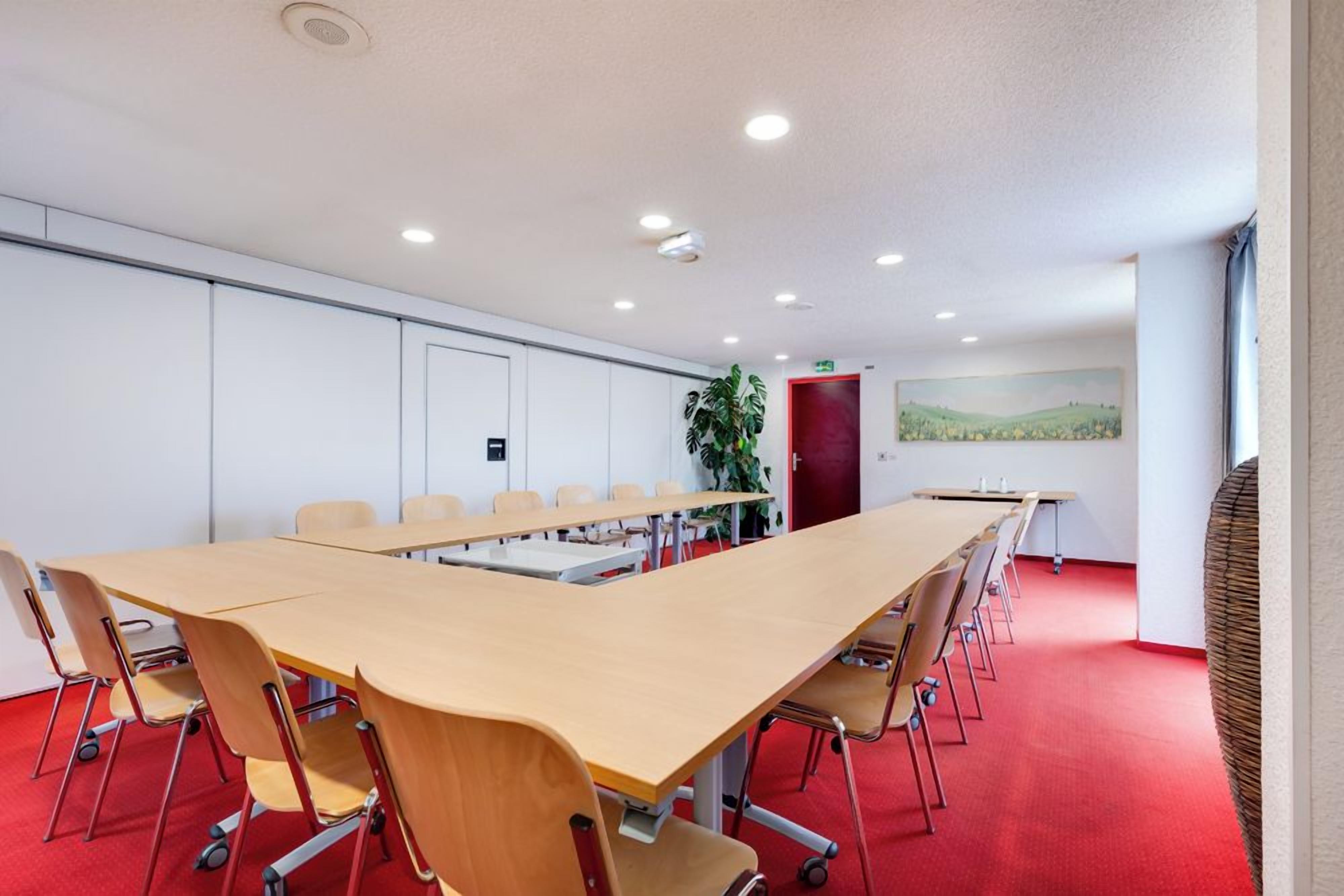 Een vergaderzaal met een lange tafel, stoelen en een roodgekleurd tapijt.
