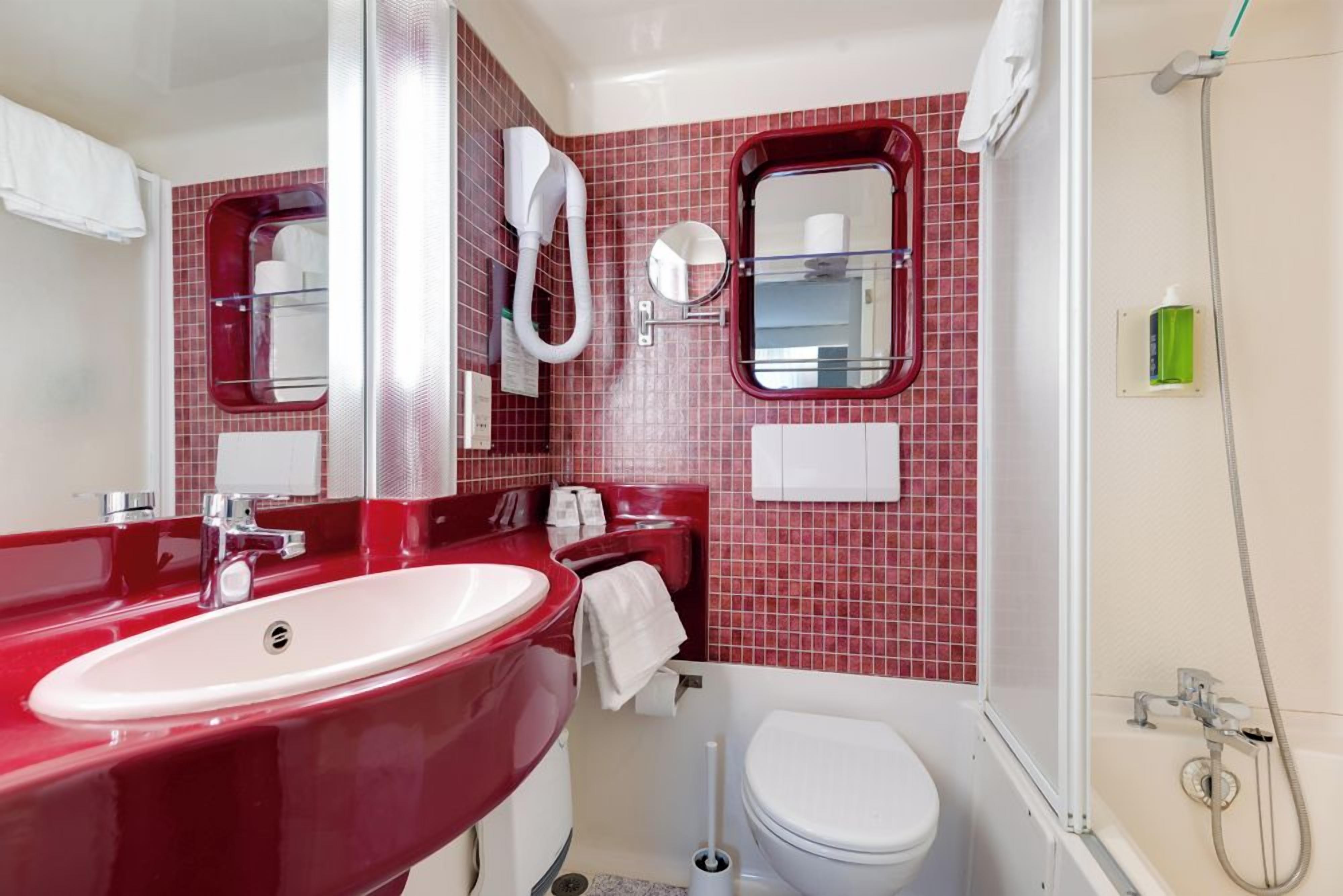 Une salle de bain avec un lavabo rouge, des toilettes blanches et un espace douche.