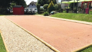 Ein großer Außenbereich mit Kiesweg und roter Fläche, möglicherweise ein Sportplatz, umgeben von Grünflächen und Gebäuden.
