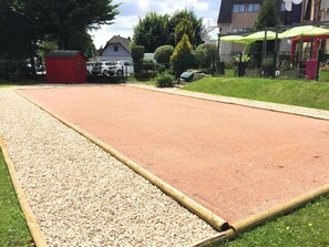 A large outdoor area with a gravel path and a red surface, possibly a sports court, surrounded by greenery and buildings. - Brit Hotel Confort Rouen Nord - Eden (Bois-Guillaume)