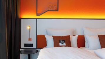 A hotel room with a bed, pillows, a nightstand, and a wall-mounted light fixture.
