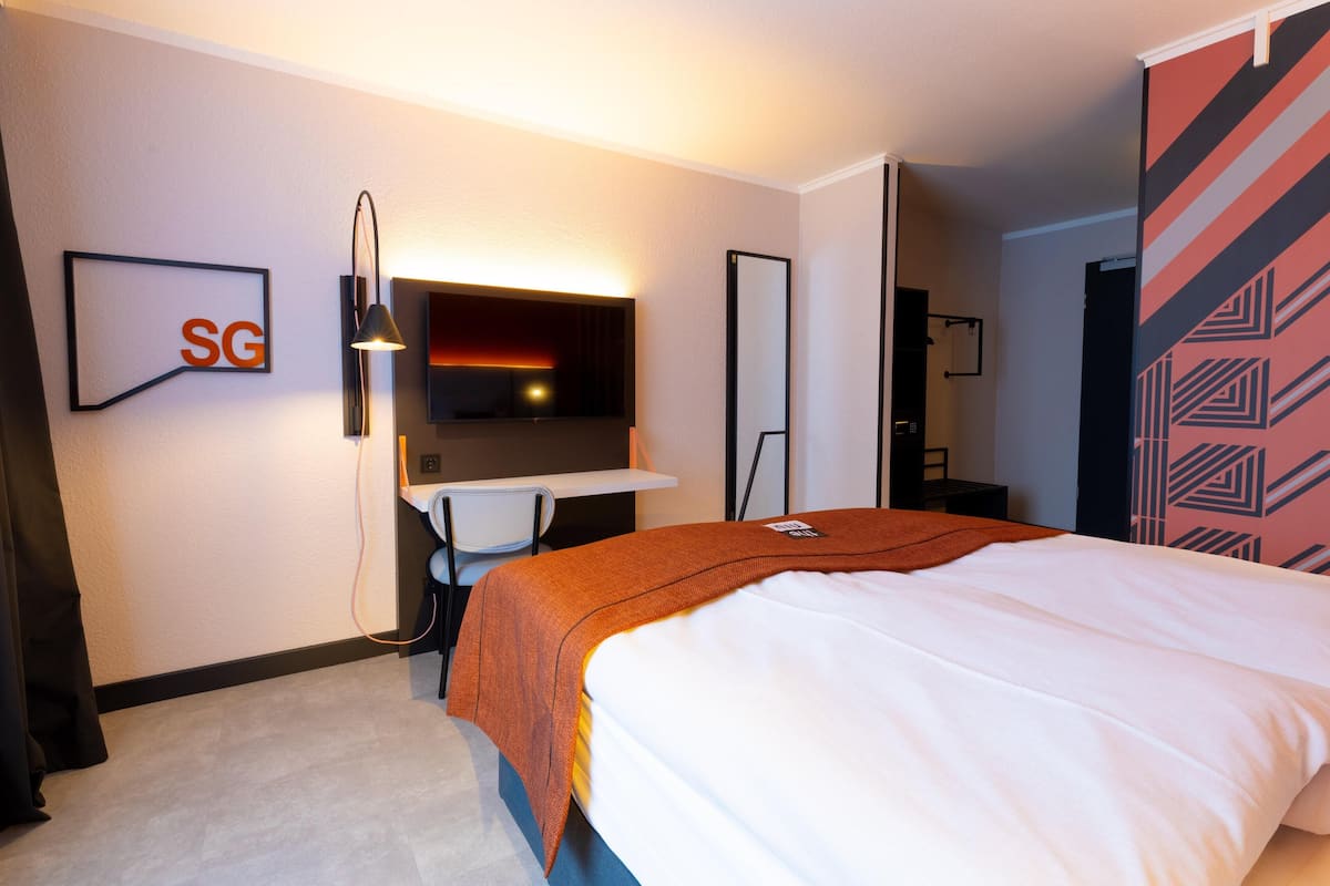 Habitación de hotel con cama, escritorio, silla, televisión y espejo instalado en la pared.