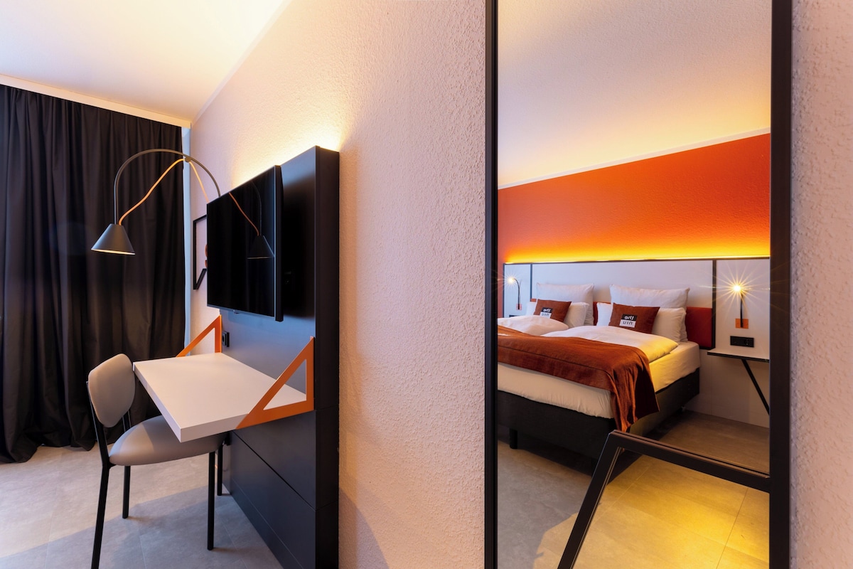 Una habitación de hotel moderna con escritorio, silla y cama con cabecera.