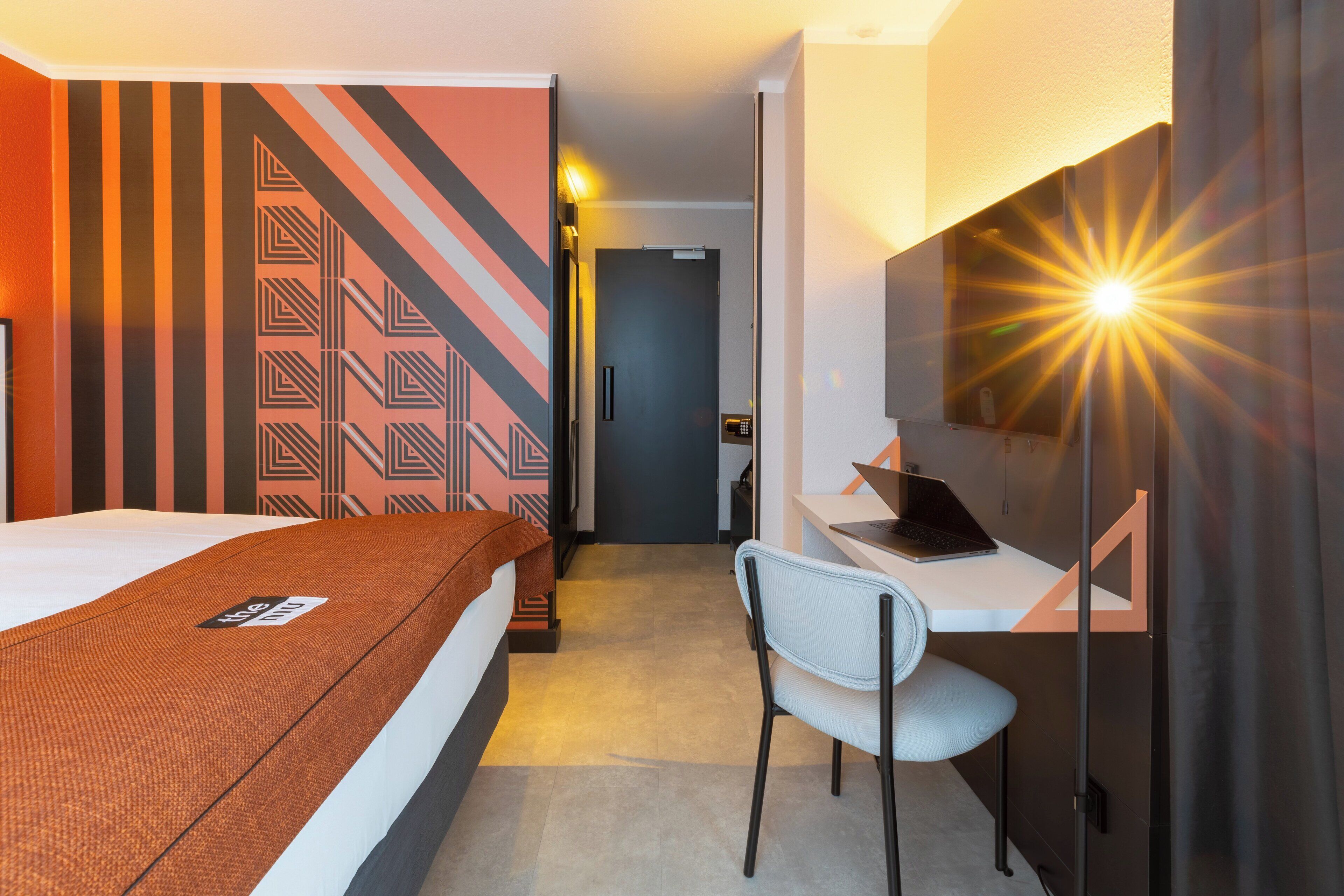 A hotel room with a bed, a desk with a laptop, a chair, and a mirror.