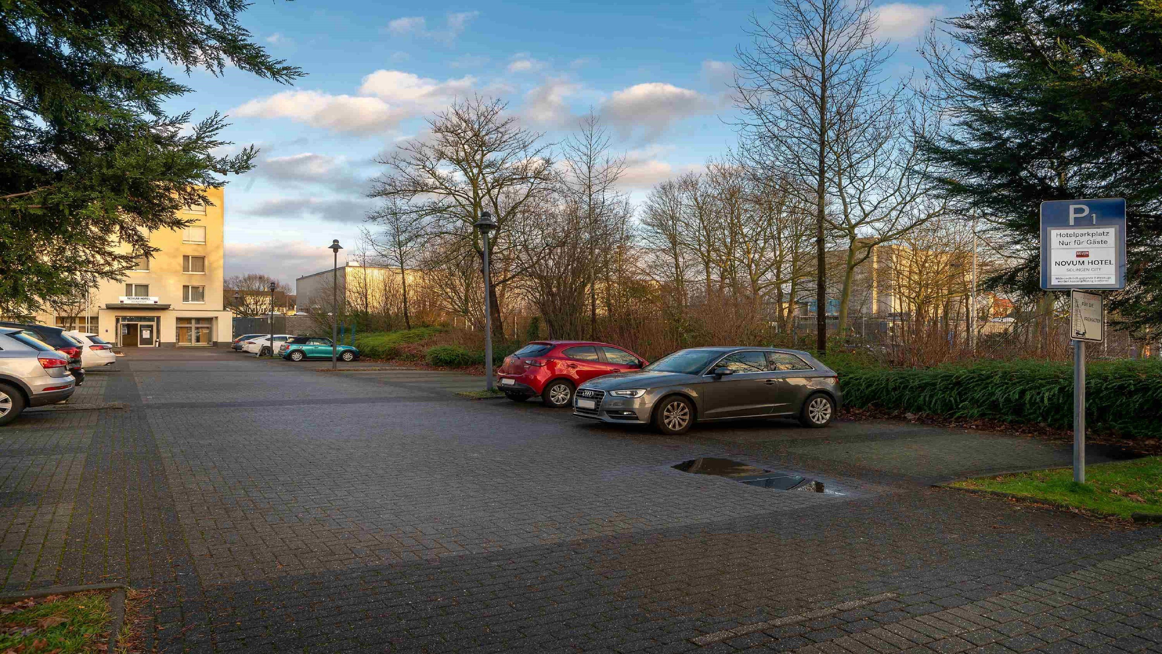 A hotel parking area with cars parked, a building with a sign, and a clear sky.