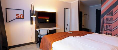 Una habitación de hotel con una cama, un escritorio, una silla, un televisor y un espejo.