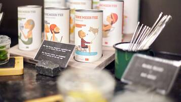A display of tea cans with illustrations and text, a black sign with white text, and a green container with metal utensils.