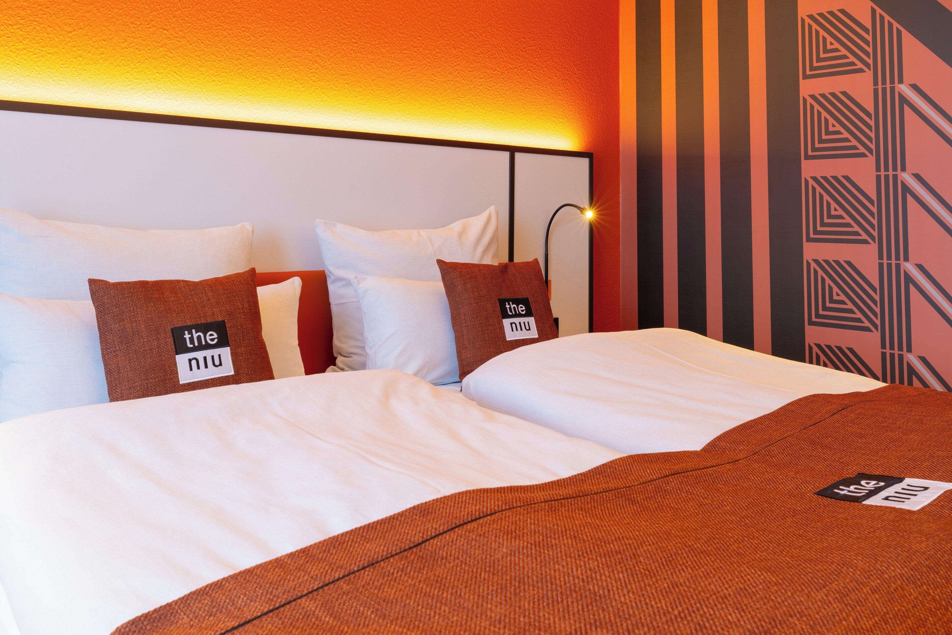 A hotel room with a large bed, two pillows with labels, a headboard, and a patterned wall.