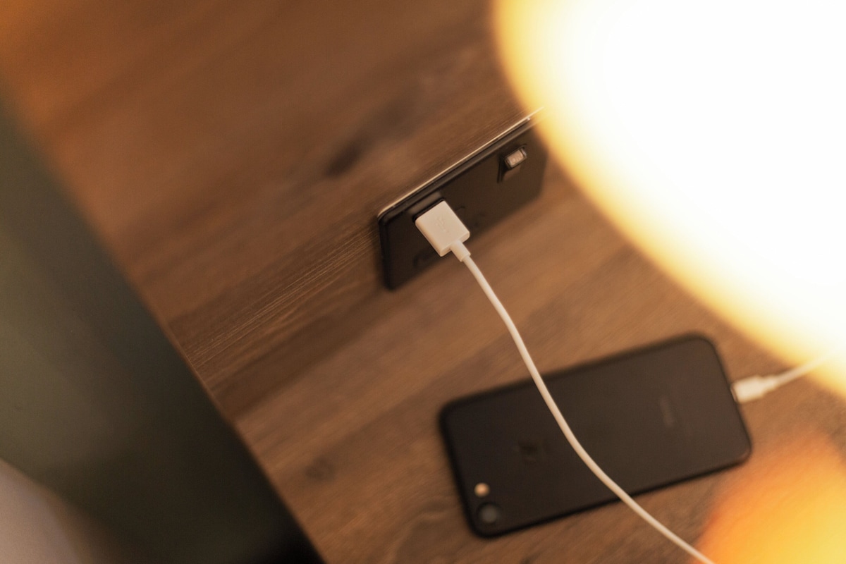 Un teléfono inteligente conectado a un cable de carga enchufado en un enchufe de pared sobre una superficie de madera.